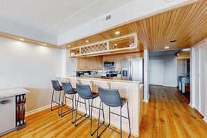 Eine moderne Küche mit Holzausstattung, einer zentralen Kochinsel mit Barhocker sowie einem sichtbaren Mikrowellenherd und Kühlschrank.