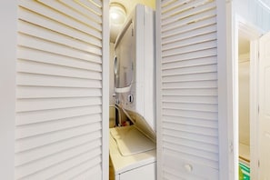 A compact, enclosed laundry area with a built-in washing machine and dryer, featuring a small countertop and storage space. - Ultimate beach getaway with ocean view, open layout, garage parking, & streaming (Ocean City)