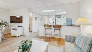 Una sala de estar moderna con sofá, televisión, mesa de comedor y zona de cocina al fondo.