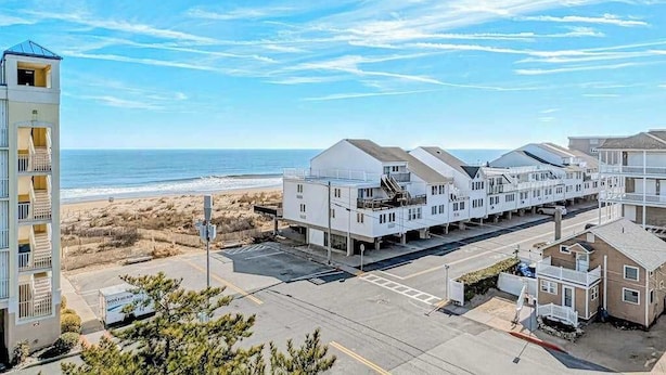 Un hotel costero con varias edificaciones blancas, un estacionamiento y vista a la playa y al océano.