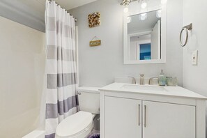 Ein Badezimmer mit Toilette, einem weißen Waschbecken, einem Spiegel mit Beleuchtung und einer Duschvorhang.