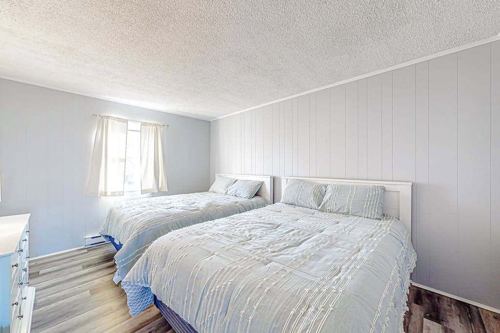 Ein Schlafzimmer mit zwei Betten, einem Fenster mit Vorhängen und Holzboden.