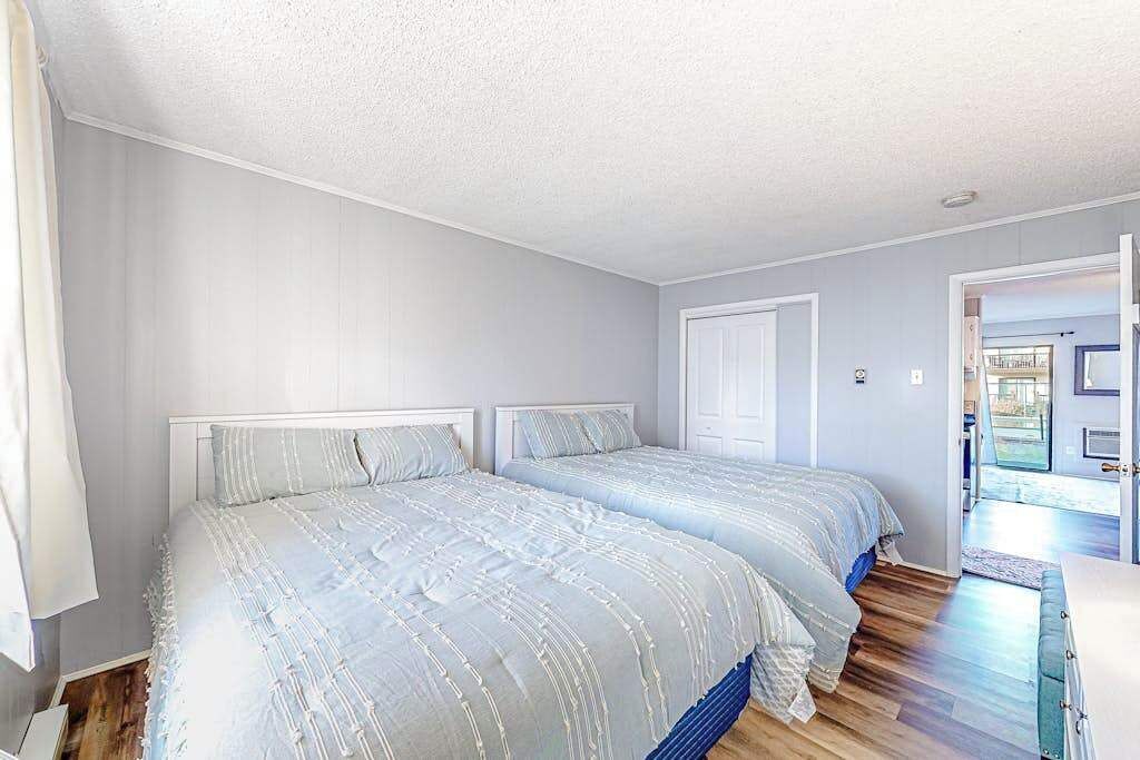 A bedroom with two beds, a white door, and a view of an outdoor area.