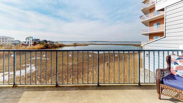 A balcony with a view of the beach, a wicker chair, and a building with balconies. - San Remo 102 (Ocean City)