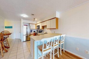 A kitchen with a central island, wooden chairs, a refrigerator, and a microwave. - San Remo 102 (Ocean City)