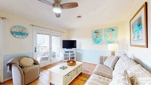 A living room with a ceiling fan, a television, a sofa, a coffee table, and wall art. - San Remo 102 (Ocean City)