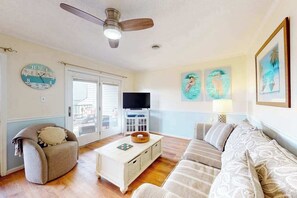 A living room with a ceiling fan, a television, a sofa, a coffee table, and wall art. - San Remo 102 (Ocean City)