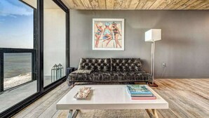 Ein modernes Wohnzimmer mit großem Fenster, einer Couch, einem Couchtisch und einem gerahmten Kunstwerk an der Wand.