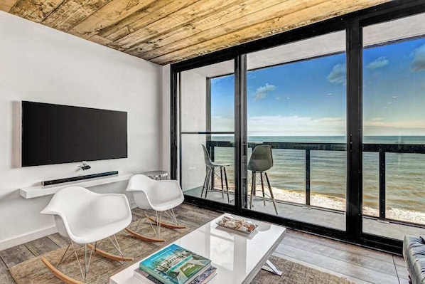 A modern room with a TV, white chairs, a coffee table, and a large window overlooking the sea. - 15th-floor oceanfront condo with pool, central AC & beach access (Ocean City)