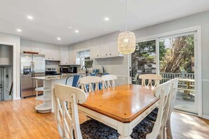 A modern kitchen with white cabinets, a wooden dining table, and a hanging light fixture. - Spacious Family Home with Full Kitchen & Deck - Close to the Beach (Ocean City)