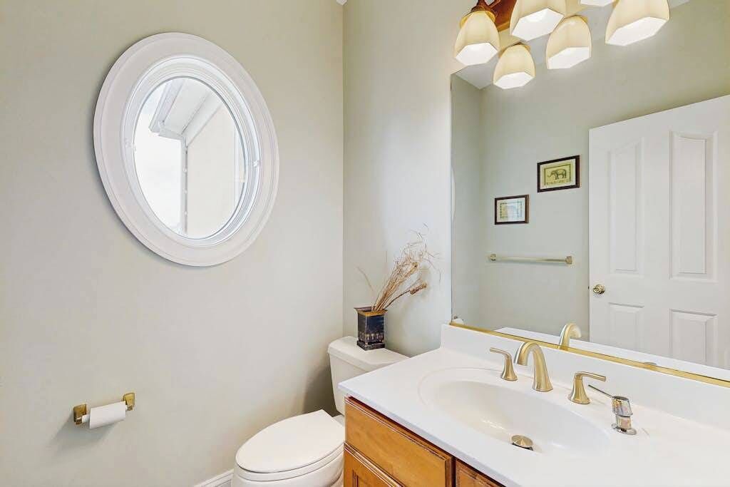 A bathroom with a round mirror, a toilet, a sink with gold fixtures, and a towel rack.