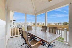 A covered outdoor area with a table and chairs, a railing, and a view of a body of water and buildings. - Heron Harbour Retreat 302 Gull Ct (Ocean City)