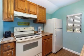 Une cuisine avec des meubles de rangement en bois, un fourneau blanc, un réfrigérateur blanc et une fenêtre avec des stores.