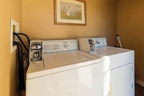 Un espace buanderie comprenant deux machines à laver et deux sèche-linge superposés, une prise de courant et un tableau accroché au mur.