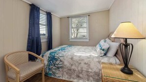 Una camera da letto con un letto, una sedia, una lampada e una finestra con persiane.
