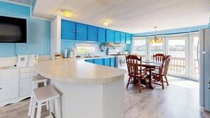Una cocina con armarios azules, una isla central, sillas de madera y un ventanal grande.