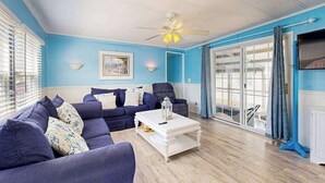 Una sala de estar con una pared azul, un ventilador de techo, una mesa de centro blanca y un sofá azul.