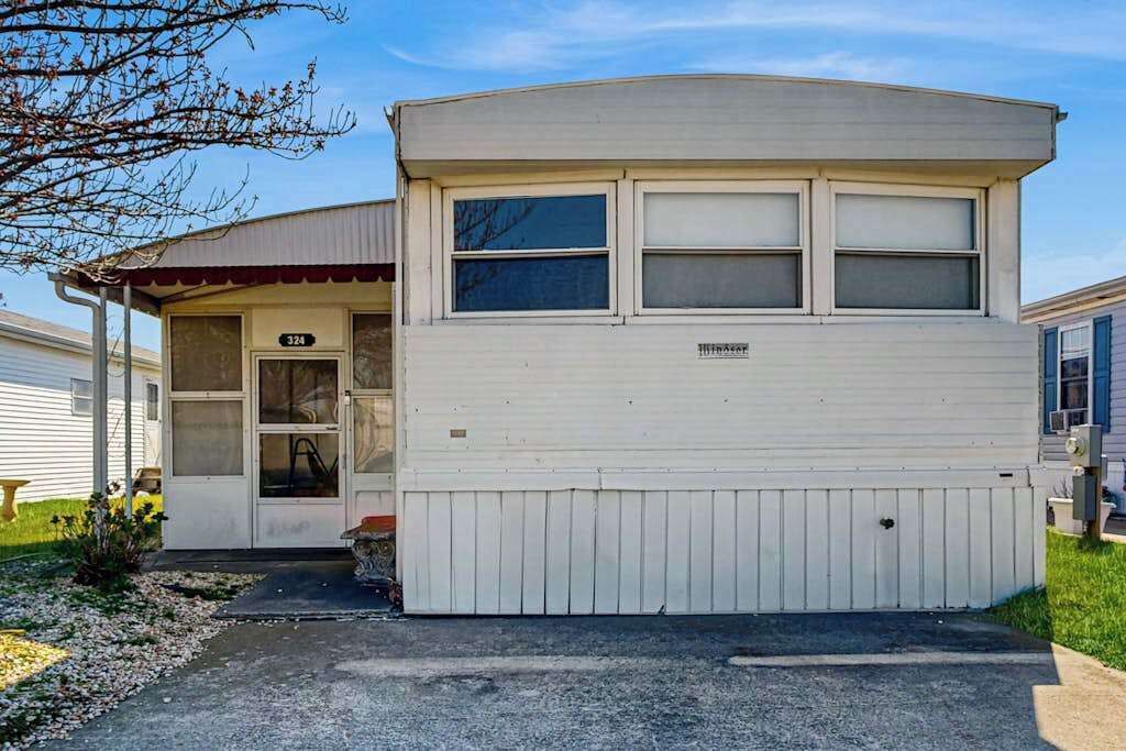 A single-story mobile home with a garage, a front door, and a small porch area.