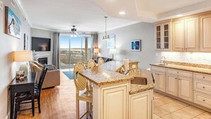 A modern kitchen with a central island, a dining area with chairs, and a view to the outside. - Belmont Towers 608 (Ocean City)