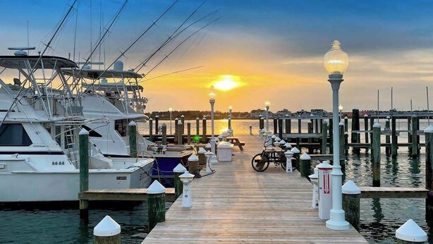 A marina with boats docked, a wooden pier, and a sunset in the background. - Belmont Towers 608 (Ocean City)
