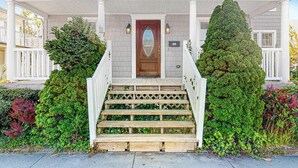 Una casa de dos pisos con un porche delantero, una puerta principal de madera y una escalera que conduce a la entrada.