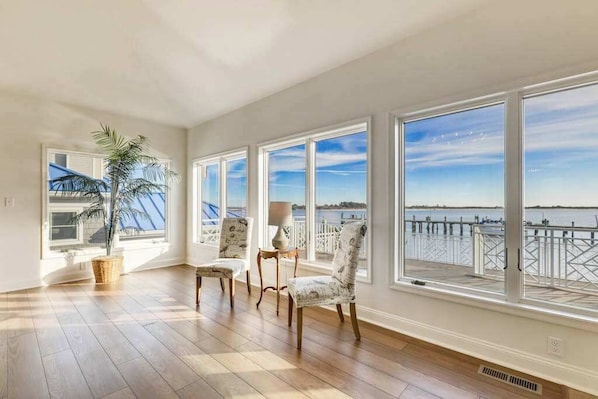 A spacious room with large windows, a wooden floor, and a view of a dock and water. - Waterfront Secured Compound in West Ocean City: Your Dream Escape (Ocean City)