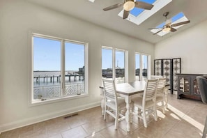 A dining area with a view of the water, large windows, ceiling fans, and a decorative cabinet. - Waterfront Secured Compound in West Ocean City: Your Dream Escape (Ocean City)