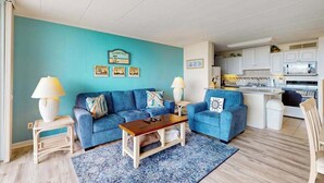 Een woonkamer met twee banken, een salontafel, en een keuken met witte kasten en apparatuur.