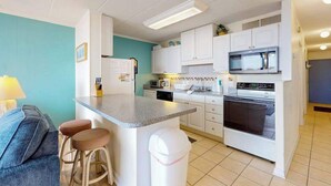 Een compacte keuken met een centraal eiland, witte kasten, een magnetron en een oven.