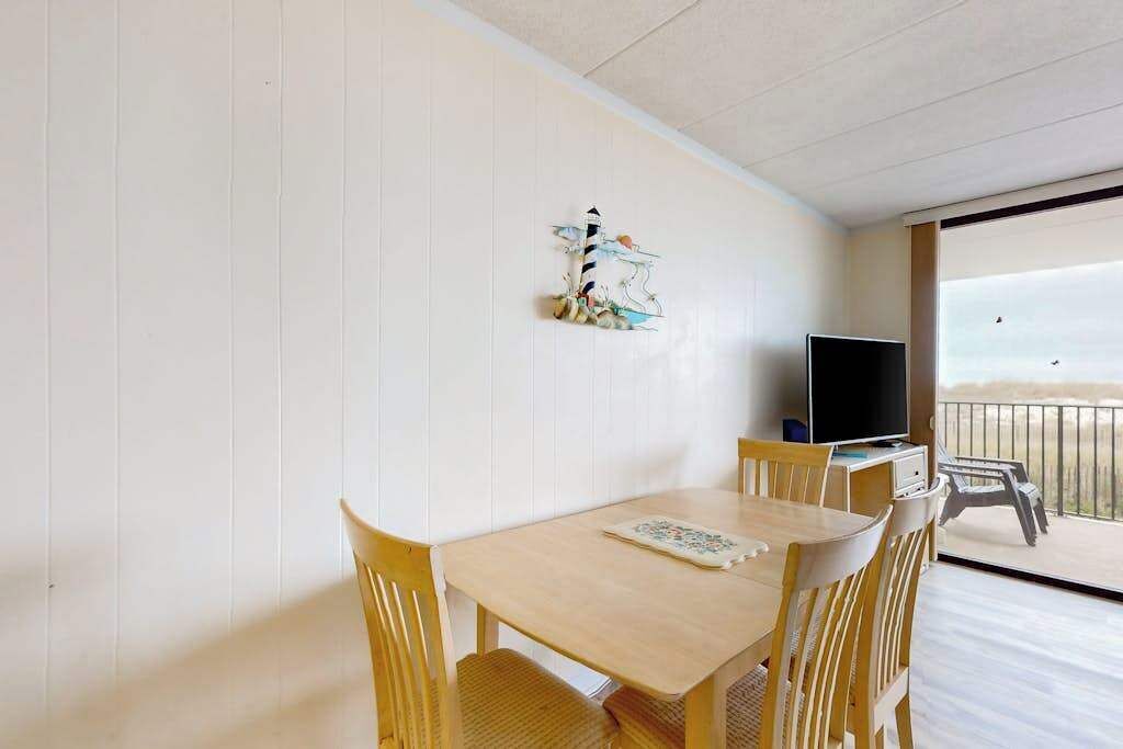 Una habitación con una mesa y sillas de madera, un televisor y un balcón con vistas.