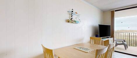 Una habitación con una mesa y sillas de madera, un televisor y un balcón con vistas.