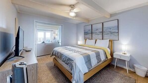 Quarto com cama, televisão, ventilador de teto, janela e obras de arte na parede.