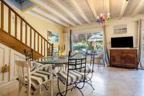 A dining area with a table, chairs, and a television. - Maison Maviela, 800 m from the ocean, Soulac (Soulac-sur-Mer)