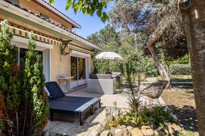 A patio with outdoor furniture, a white umbrella, and a view of the surrounding garden. - Maison Maviela, 800 m from the ocean, Soulac (Soulac-sur-Mer)
