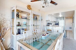 Eine moderne Küche mit weißen Schränken, ein Essbereich mit einem Glastisch und Korbstühlen sowie ein Deckenventilator.