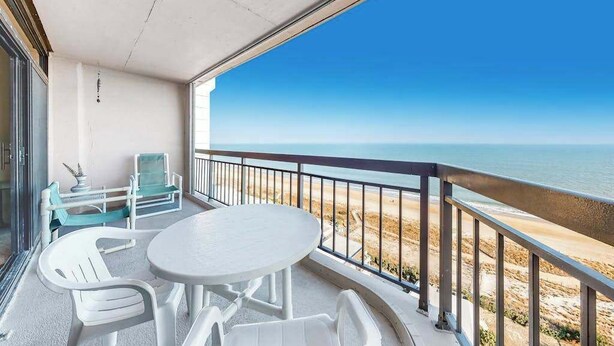 Ein Balkon mit Tisch und Stühlen mit Blick auf einen Strand.