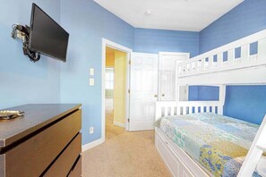 Quarto com cama de solteiro, escrivaninha com cadeira, televisão de tela plana fixada na parede e porta que dá para outro cômodo.