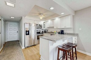 A modern kitchen with white cabinets, stainless steel appliances, and a granite countertop. - Oceanfront Mooring Condo w/ WiFi, W/D, Ocean View, AC - Sun, Sand & Surf Await (Ocean City)