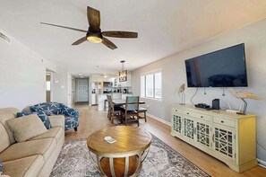 A spacious living area with a ceiling fan, a flat-screen TV, a dining table, and a kitchen in the background. - Oceanfront Mooring Condo w/ WiFi, W/D, Ocean View, AC - Sun, Sand & Surf Await (Ocean City)