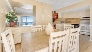 A modern kitchen with white cabinets, a dining table with chairs, and a view of the ocean. - High Point South P10 (Ocean City)