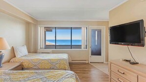 A room with two beds, a TV, a dresser, and a large window with a view of the beach. - High Point South P10 (Ocean City)
