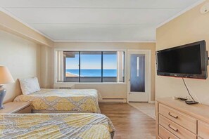 Ein Zimmer mit zwei Betten, einem Fernseher, einer Kommode und einem großen Fenster mit Blick auf den Strand.