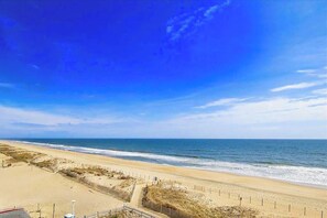Ein Strand mit blauem Himmel, sandigem Ufer und einer Umzäunung am Wasser.