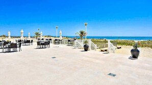 An outdoor terrace with tables and chairs, a palm tree, and a view of the beach. - Gateway Grand 507 (Ocean City)