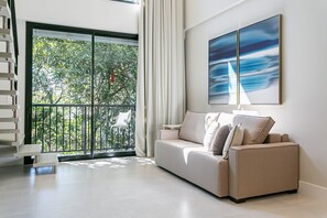 Uma sala de estar moderna com sofá, pintura e varanda com vista para o verde.
