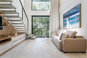 Uma sala de estar moderna com escada, sofá, mesa de centro e uma janela grande com vista para o verde.