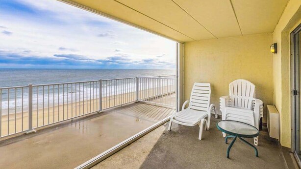 Ein Balkon mit Blick auf das Meer, zwei weiße Stühle und ein kleiner Tisch.