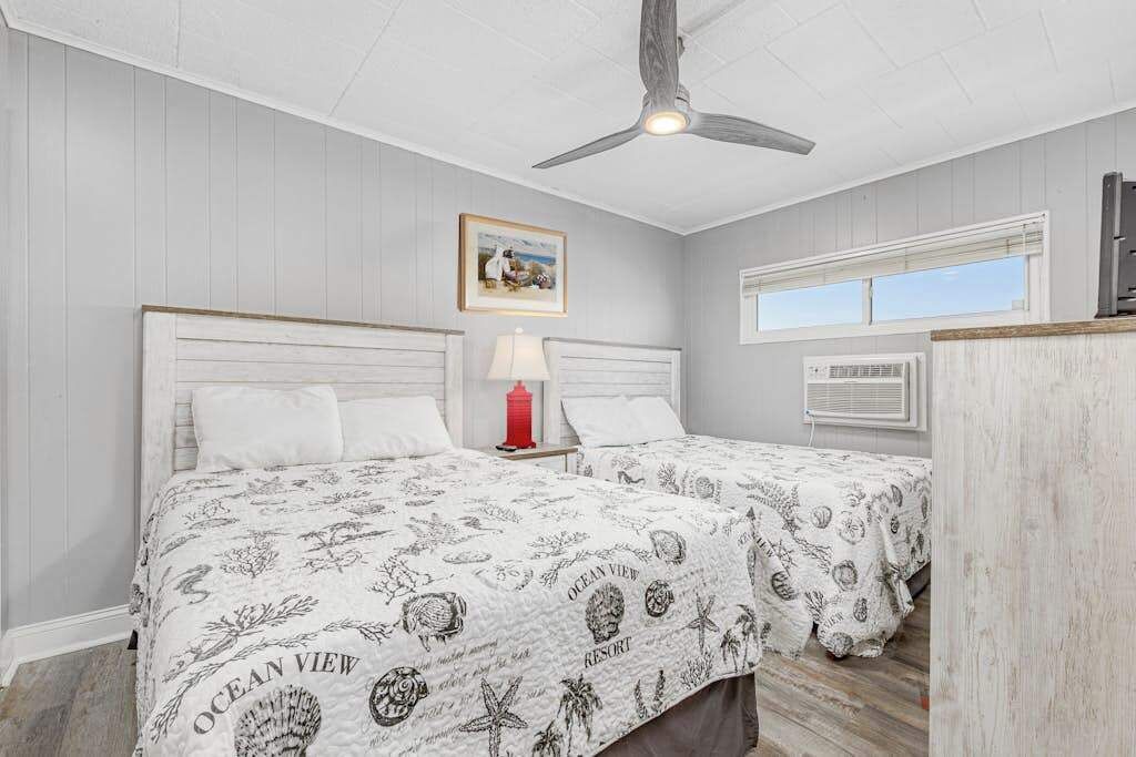 Une chambre à coucher avec un lit, un ventilateur de plafond, une fenêtre et un tableau au mur.