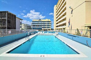 A swimming pool with a 8ft depth marker, surrounded by buildings, and a clear sky. - Oceanfront Calypso Condo w/ Ocean View Balcony, WiFi, Laundry & Shared Pool (Ocean City)