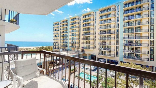 Un balcone con vista su un edificio a più piani, una piscina e l'oceano.